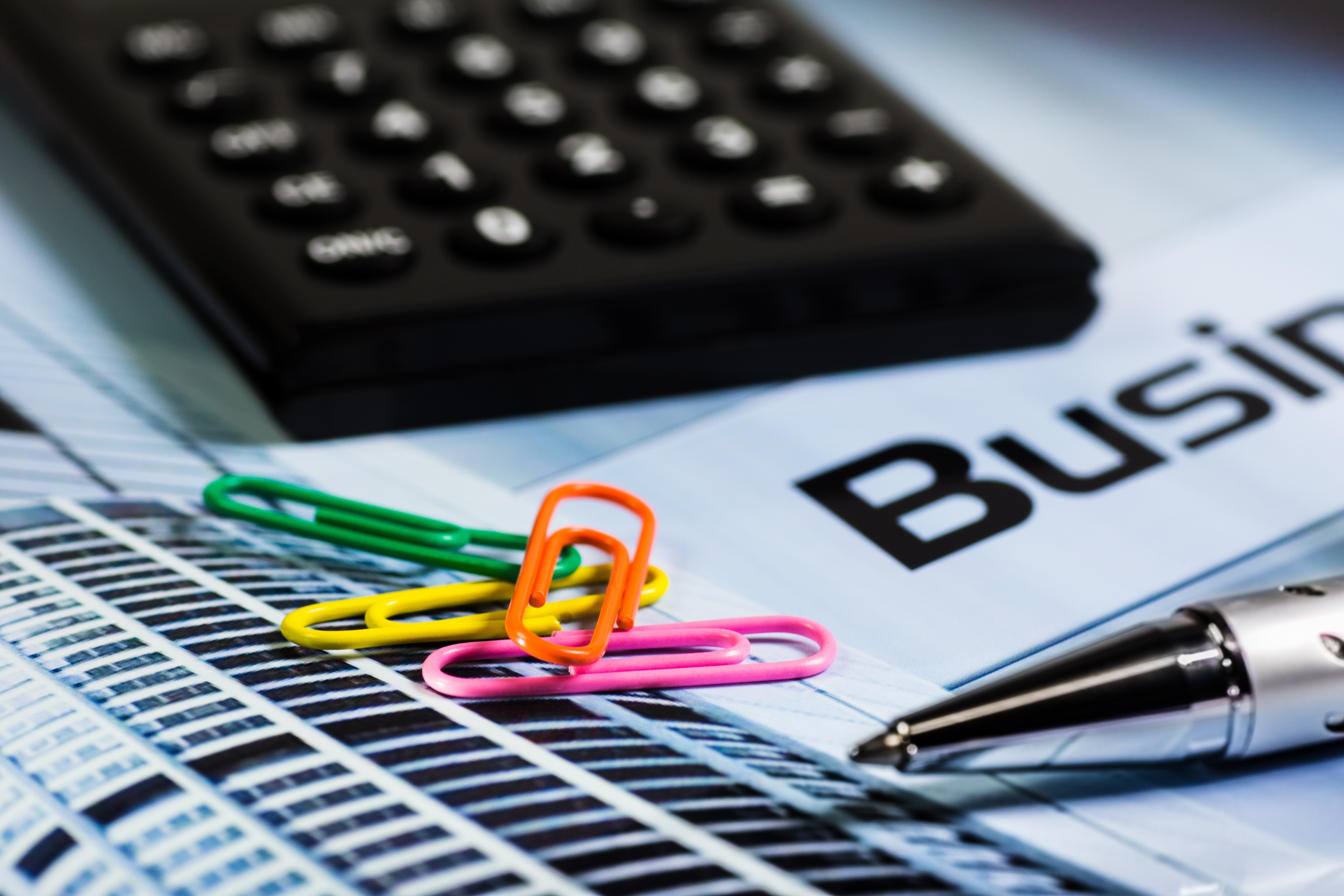 Informative calculation Calculator, colorful staples, ballpoint pen and a document that says Business
